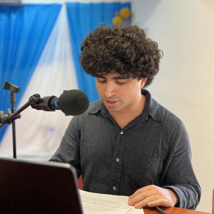 A young man with frizzy hair reading a paper at a conference.